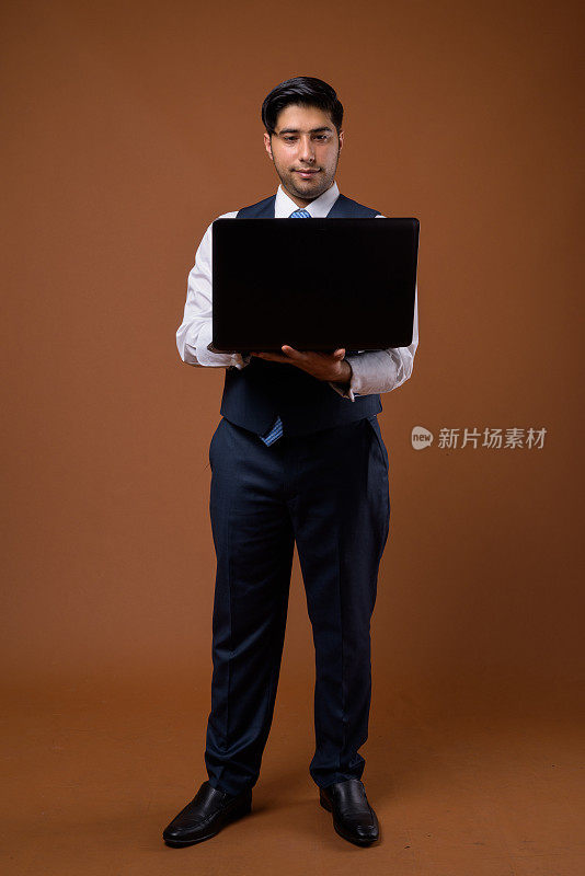 工作室拍摄的年轻英俊的伊朗商人使用笔记本电脑的彩色背景