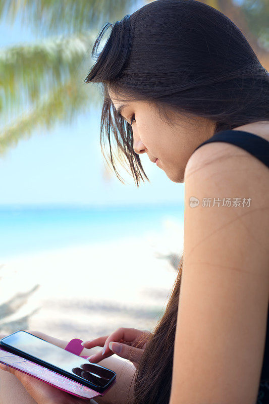 少女在夏威夷海滩上的椰子树下使用手机