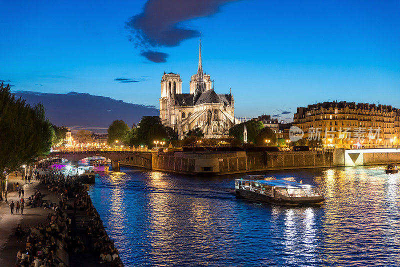 巴黎圣母院与游船在塞纳河上的夜晚，法国巴黎