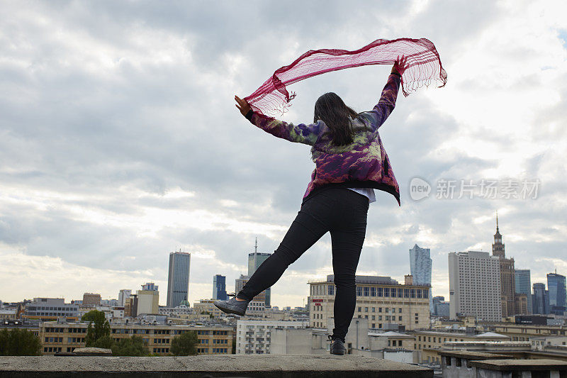 伸开双臂迎着风。在屋顶上保持平衡的亚洲妇女