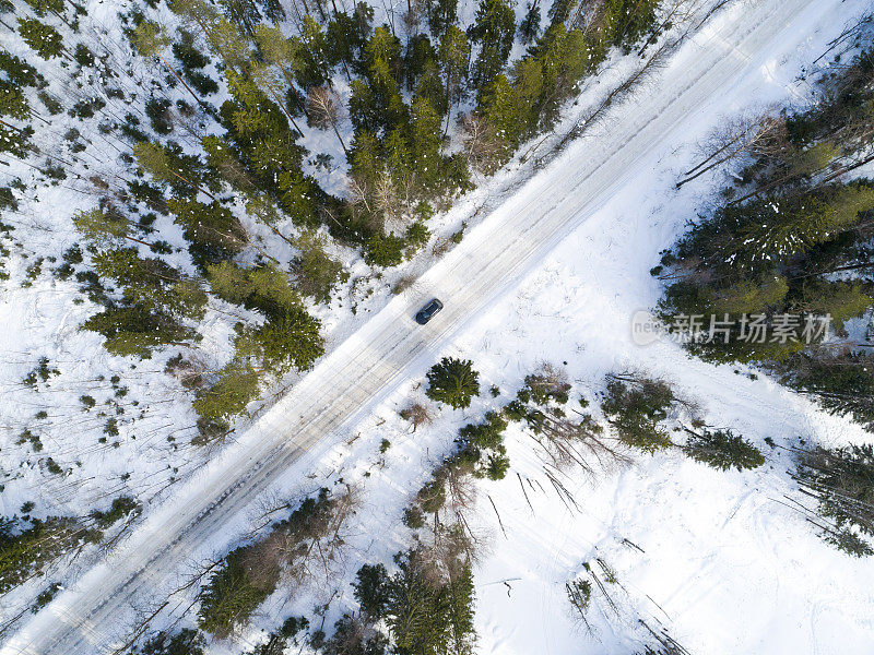 一辆汽车在冬季道路上的鸟瞰图。冬天的乡村景观。空中拍摄的雪林与一辆汽车在道路上。无人机从上面拍下的。航拍照片。四轴飞行器。空中汽车视图