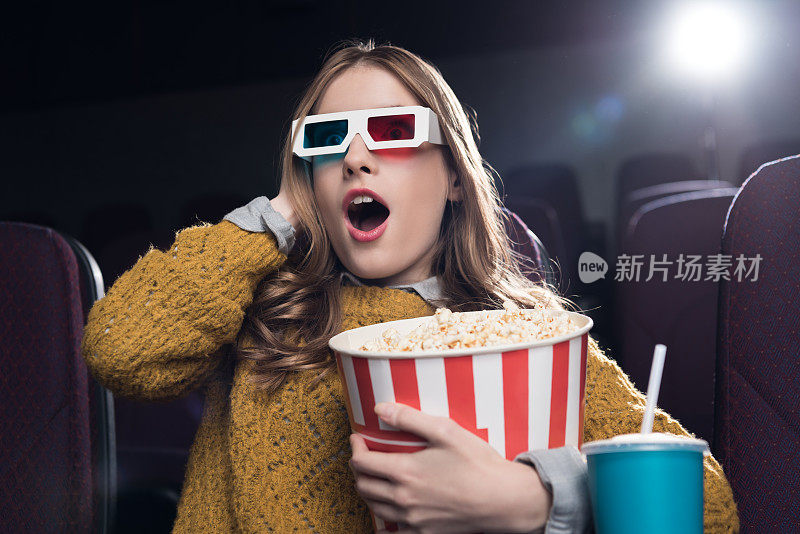 兴奋的女人戴着3d眼镜，拿着一大篮爆米花在电影院看电影