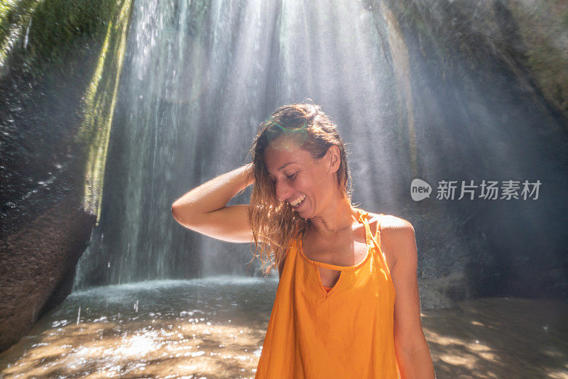 穿着黄色衣服的女孩站在热带雨林的洞穴里，仰望着从岩石上射下来的壮观的阳光。人们旅行的奇妙欲望自然的概念