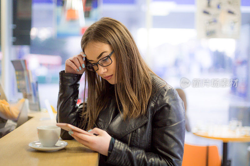 年轻女子在喝咖啡休息时间玩智能手机