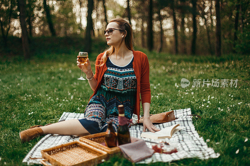 时尚的女人在大自然的野餐上喝葡萄酒