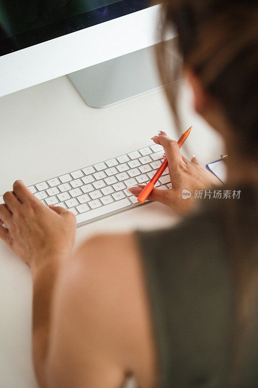 一个女人在办公桌旁拿着笔在键盘上打字