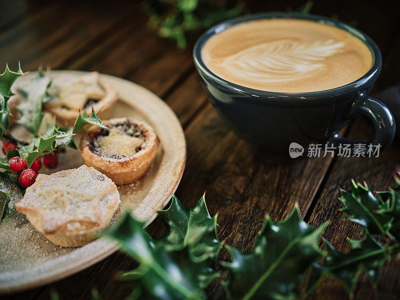 一杯白咖啡，一盘肉馅饼，放在一张放着冬青的深色老木桌上。