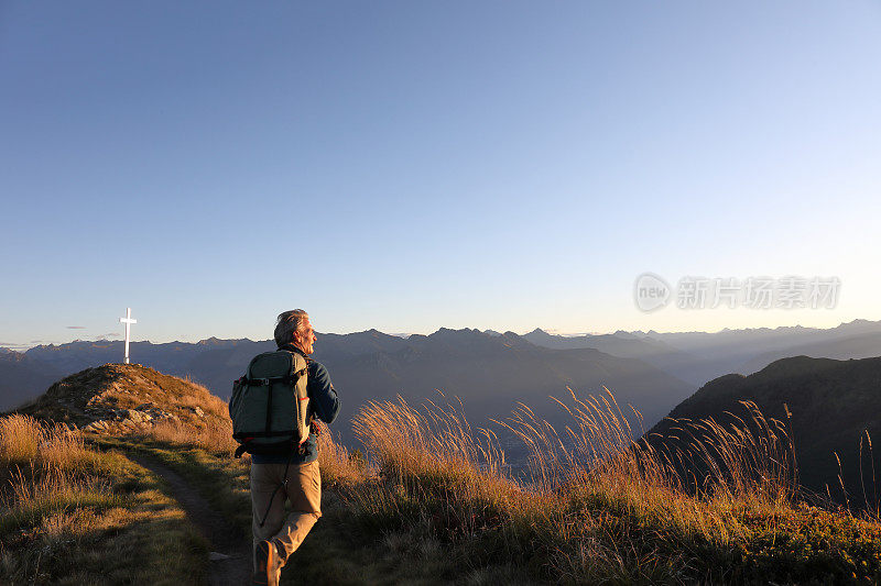 日出时，人们沿着长满草的山脊徒步旅行