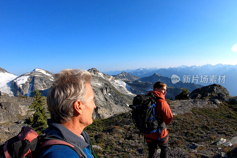 登山运动员在日出时沿着多岩石的峰顶徒步旅行