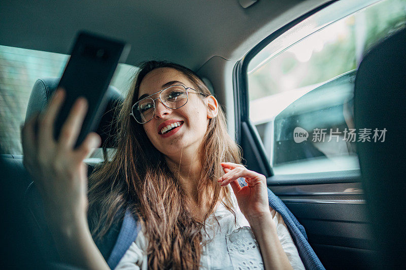 女商人坐在汽车后座上用智能手机自拍