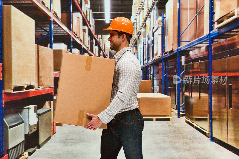 一名男性体力劳动者戴着头盔，手持纸箱站在商品前的储物柜前