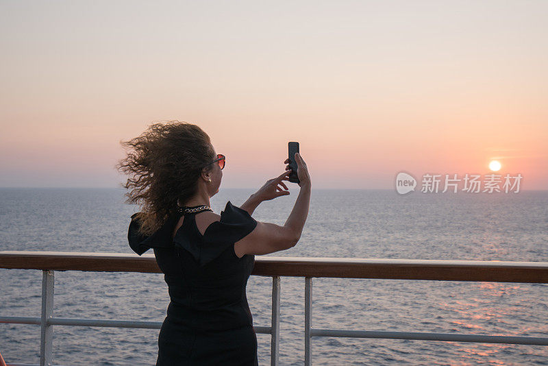 美丽的女人站在游轮甲板上，在夕阳下自拍。