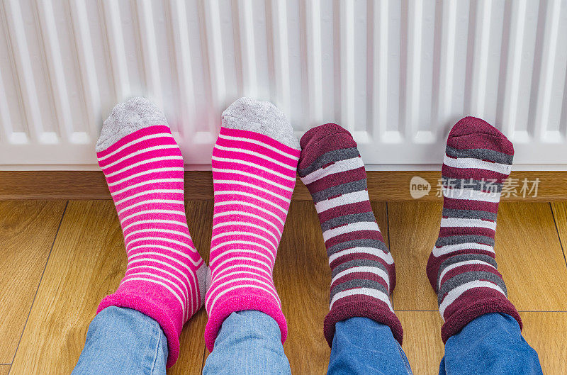 冬天的时候，一家人穿着一双色彩鲜艳的冬天袜子，在暖气片前暖脚。家里的电或煤气加热器。家中供暖季节的象征形象。