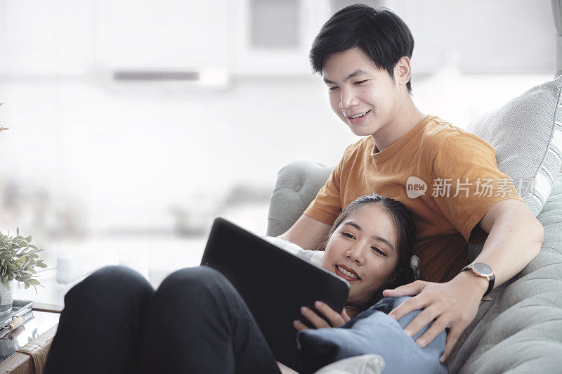 美丽的年轻相爱的夫妇使用平板电脑，一起度过美好的时光在家里的客厅与幸福。