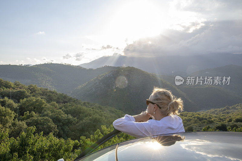 女人放松对汽车在繁茂的山谷在日出