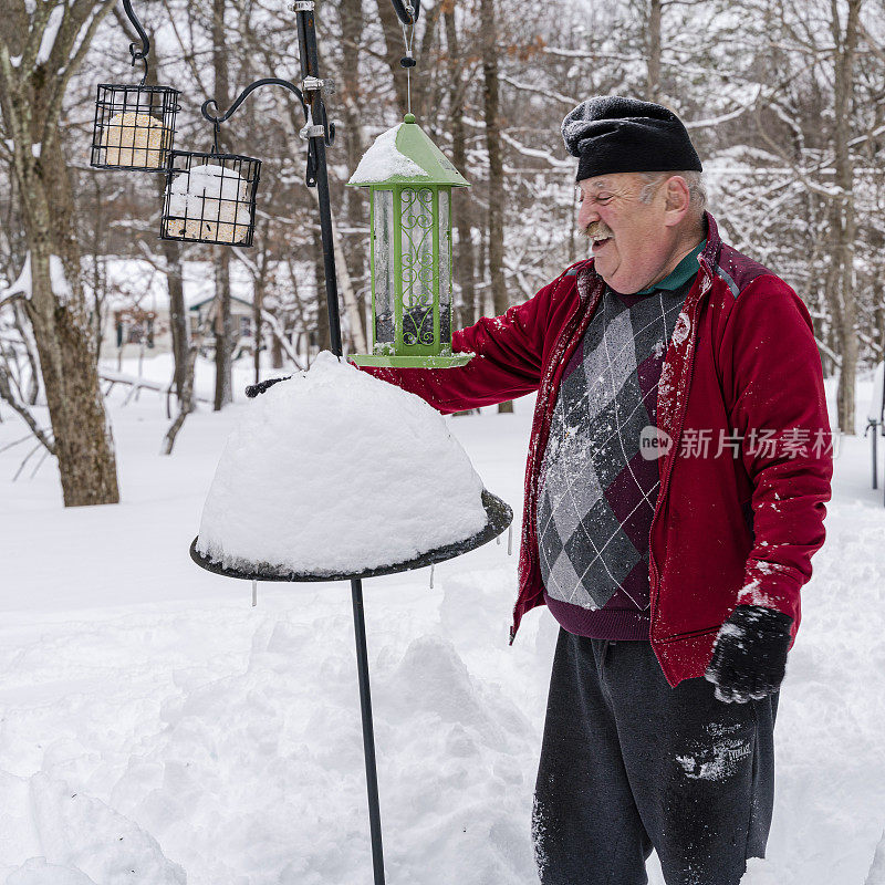 一场冬季降雪后，一位退休老人正在清理雪地里的喂鸟器。