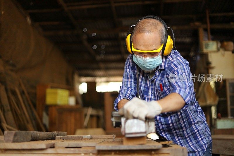 年长的亚洲木匠在他自己的车库风格的车间里使用木板手工刨床，在退休的年龄，爱好与复印空间