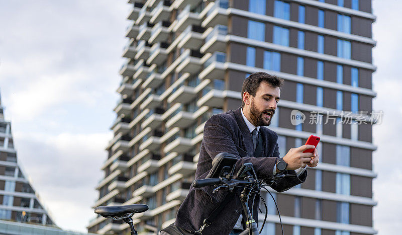 一个年轻时尚的商人骑自行车上班，用手机发短信。一个快乐微笑的男人在大街上用智能手机骑着自行车。