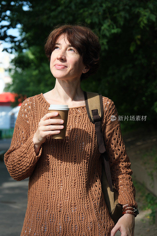 成熟的女人在城市的大街上等着用纸杯喝咖啡