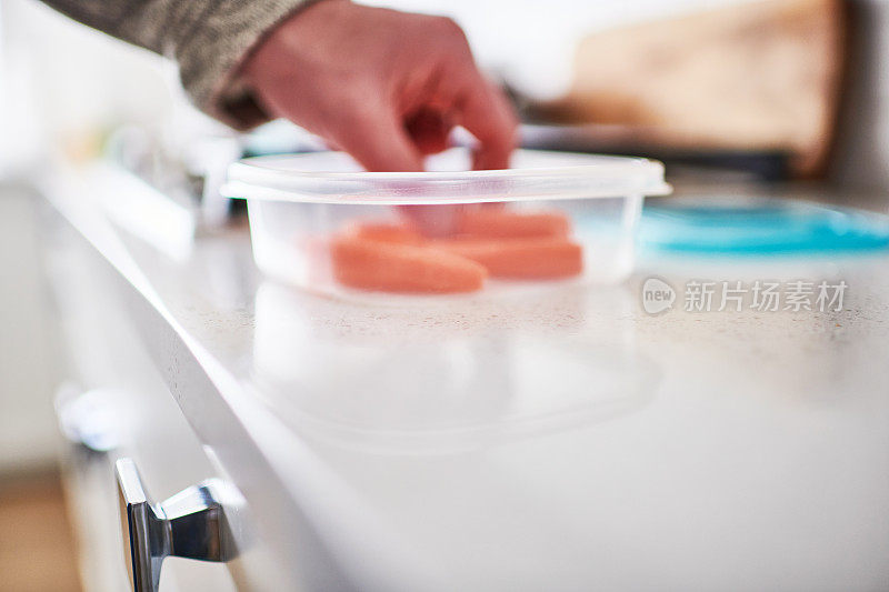 在明亮的现代厨房里，不明身份的男性从可重复使用的塑料容器里吃食物