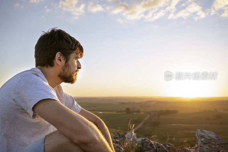 夕阳西下时，一个年轻人站在山顶眺望地平线。想象未来。