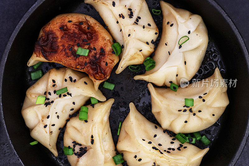 这是一个南亚饺子的特写，在油煎锅里，用白面粉和水面团填满鸡肉和混合蔬菜，点缀韭菜和黑种，黑色的背景，俯瞰的视角