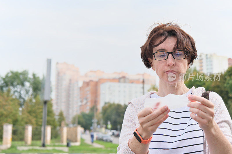 成熟的女人站在城市的街道上，手里拿着湿纸巾