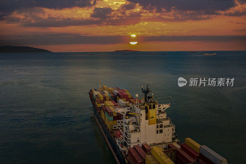 载货集装箱船在日落时离开港口，
