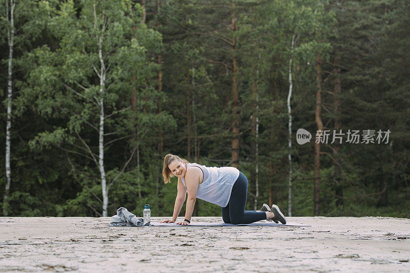 一个超重的女人在户外的瑜伽垫上伸展身体