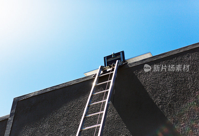 金属梯子在阳光下闪闪发光，通向屋顶上的太阳能电池板