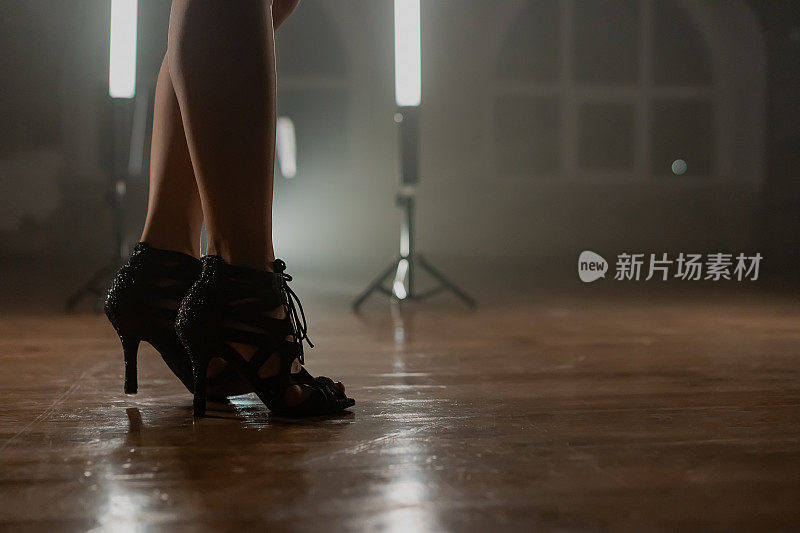 穿着高跟鞋的女人站在烟雾缭绕的舞蹈室里，手里拿着灯。双腿修长的女孩。现代编舞，女性鞋的概念。