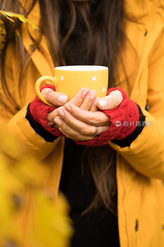 秋天的森林里，穿着黄色皮大衣的女人手里拿着黄色的茶杯。