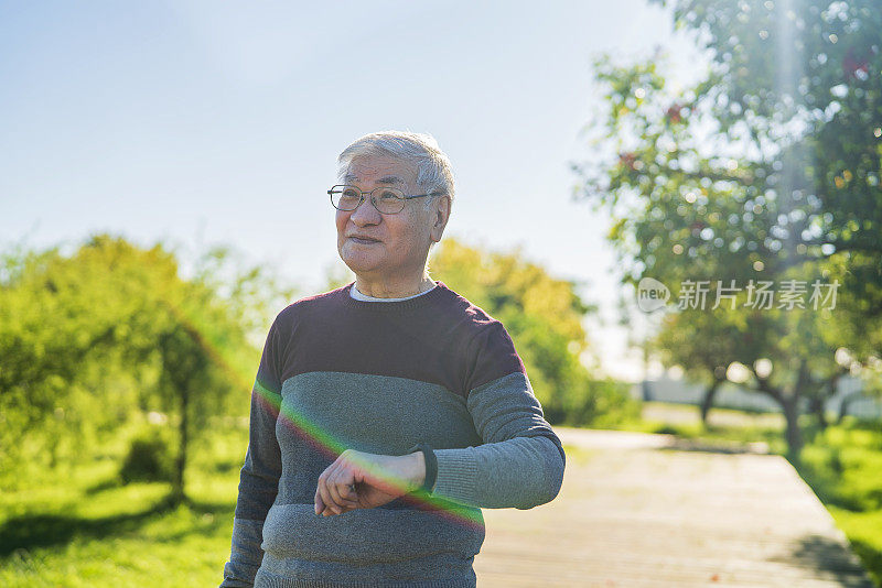 亚裔美国成熟男性在公园散步时用智能手表计时