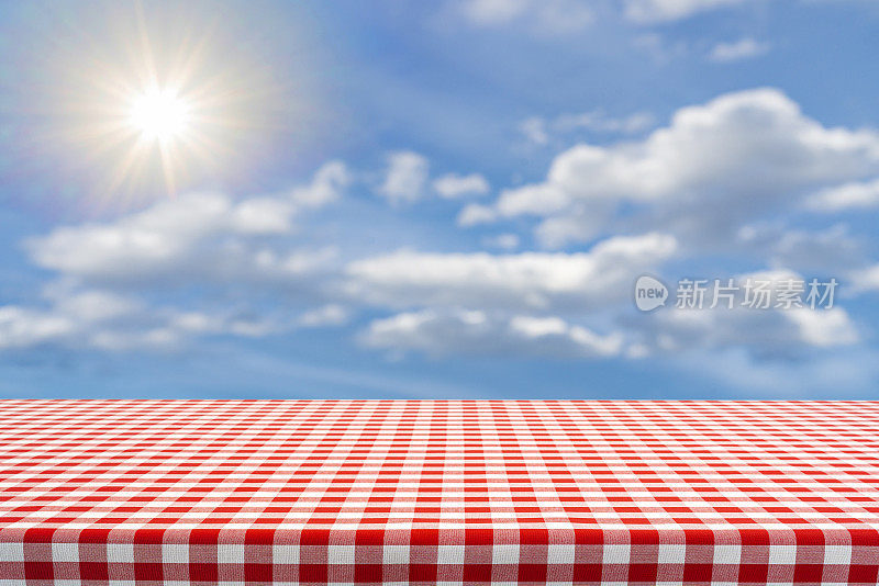 空空如也的餐桌，铺着野餐毯，背景是蓝天