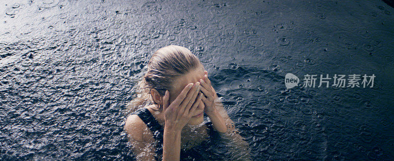 柔弱的女子从黑暗的水中冒出来，享受着雨。自然美容护理隐喻