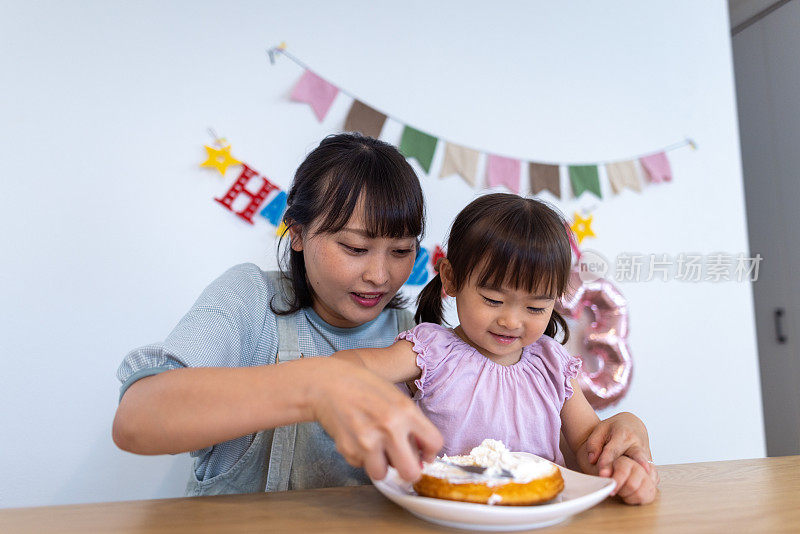 母女俩在家把奶油涂在生日蛋糕上