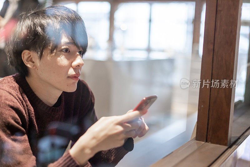 一名20多岁的男子在咖啡厅窗口操作智能手机