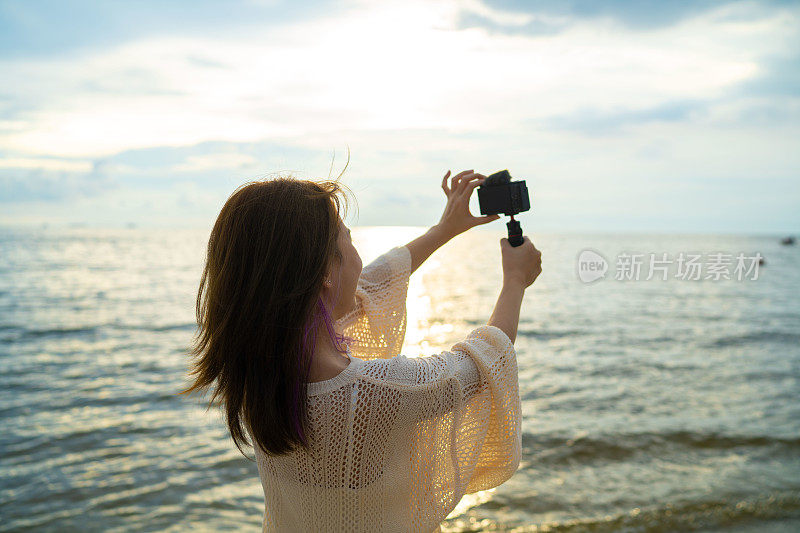 美丽的亚洲女人用相机拍摄海景，所以可以记住这一刻。