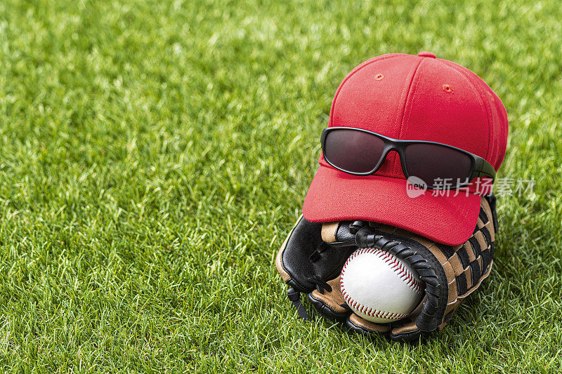草地上一个戴着手套的新棒球，上面戴着棒球帽和太阳镜