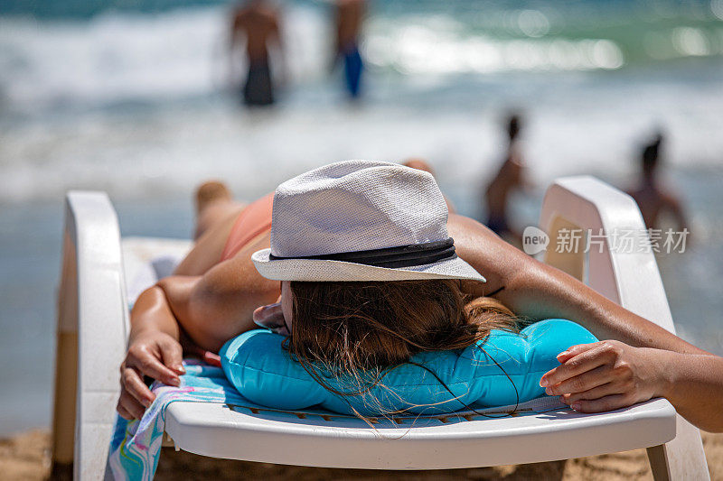 难以辨认的斜躺的女人与白色的帽子在海滩日光浴的背景下的大海，特写