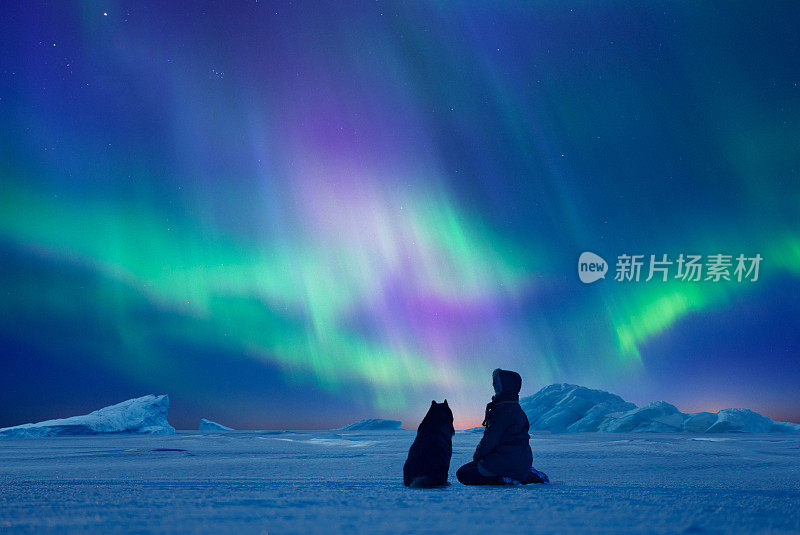 一个女人带着她的狗欣赏北极光。北极光在北极的冬季景观。