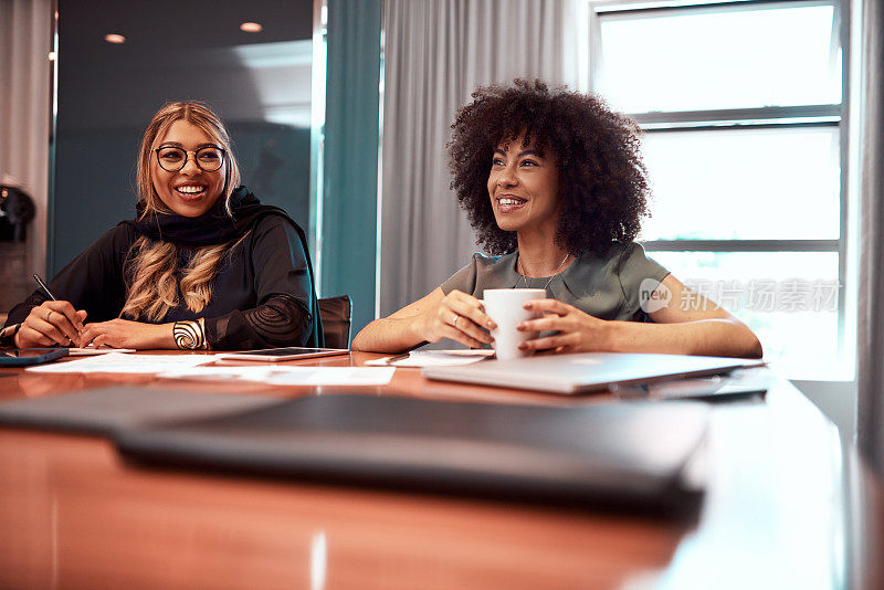 快乐，微笑的女人在会议室进行友好的讨论。女性围坐在桌子旁的支持性企业业务。企业职业女性在会议后放松