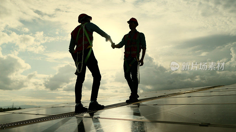 工程师或技术人员与承包商或合作伙伴穿着安全制服，在一起工作后握手完成或成功处理安装、检查工作系统和维修屋顶太阳能发电厂的太阳能电池板的雇用。