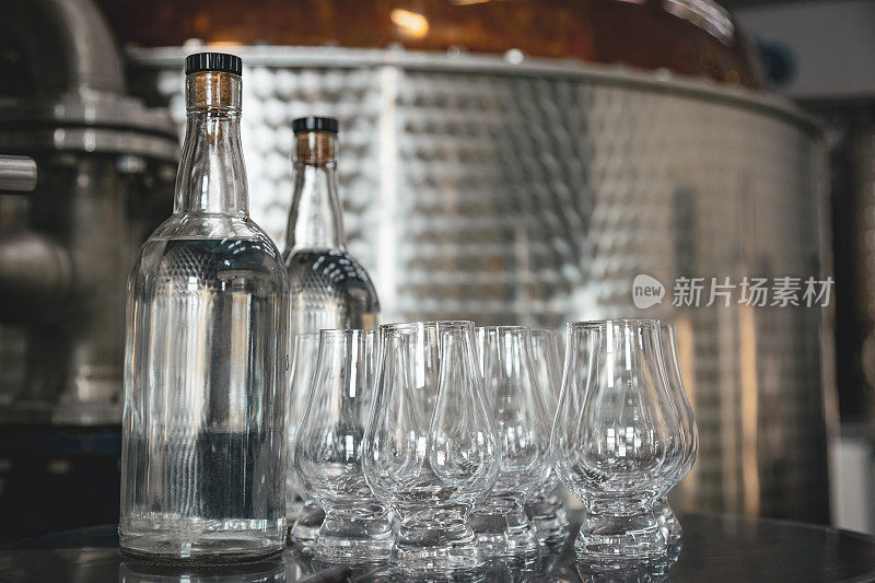 现代酒厂设备。威士忌生产用工业设备在铜真空蒸馏器前品尝威士忌烈酒的玻璃杯。
