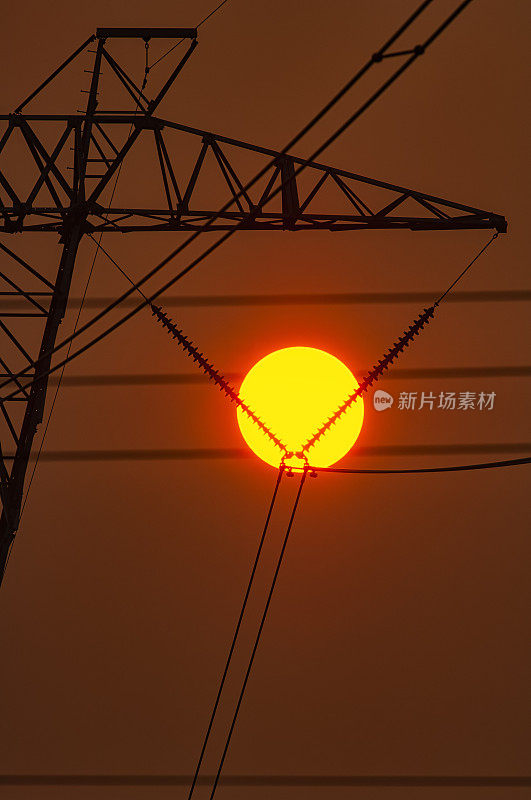 一个炎热的夏天，太阳在高压输电塔后面的特写