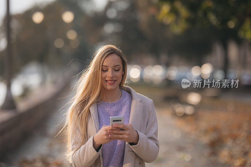 微笑的年轻女子在街上使用智能手机