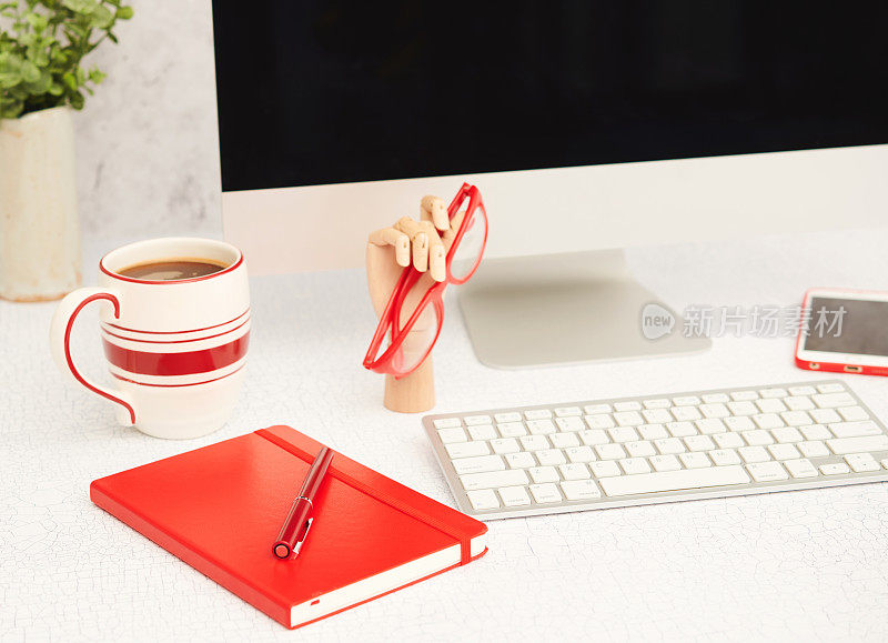 明亮的办公环境，配有台式电脑和红色办公用品。咖啡杯，笔记本和钢笔