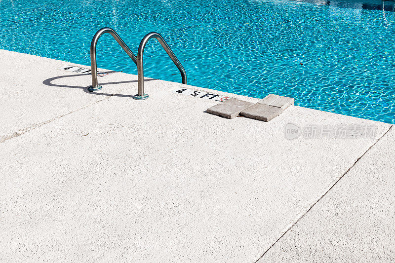 在阳光明媚的日子里，空的室外游泳池配有梯子
