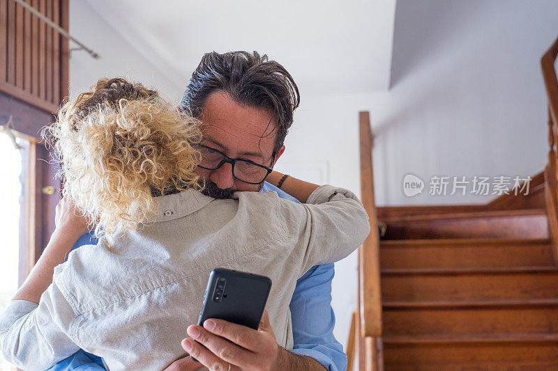 出轨男子在家拥抱妻子时，用手机给爱人发短信。一个成熟的男人背着女朋友在智能手机上秘密聊天。丈夫被手机分心