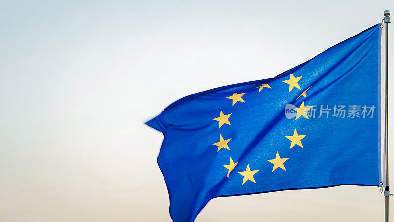 欧洲联盟旗或欧洲旗帜，蓝色背景上有十二颗金色的星星，代表欧洲人民的联盟。天空背景上的旗杆上飘扬的欧盟旗帜